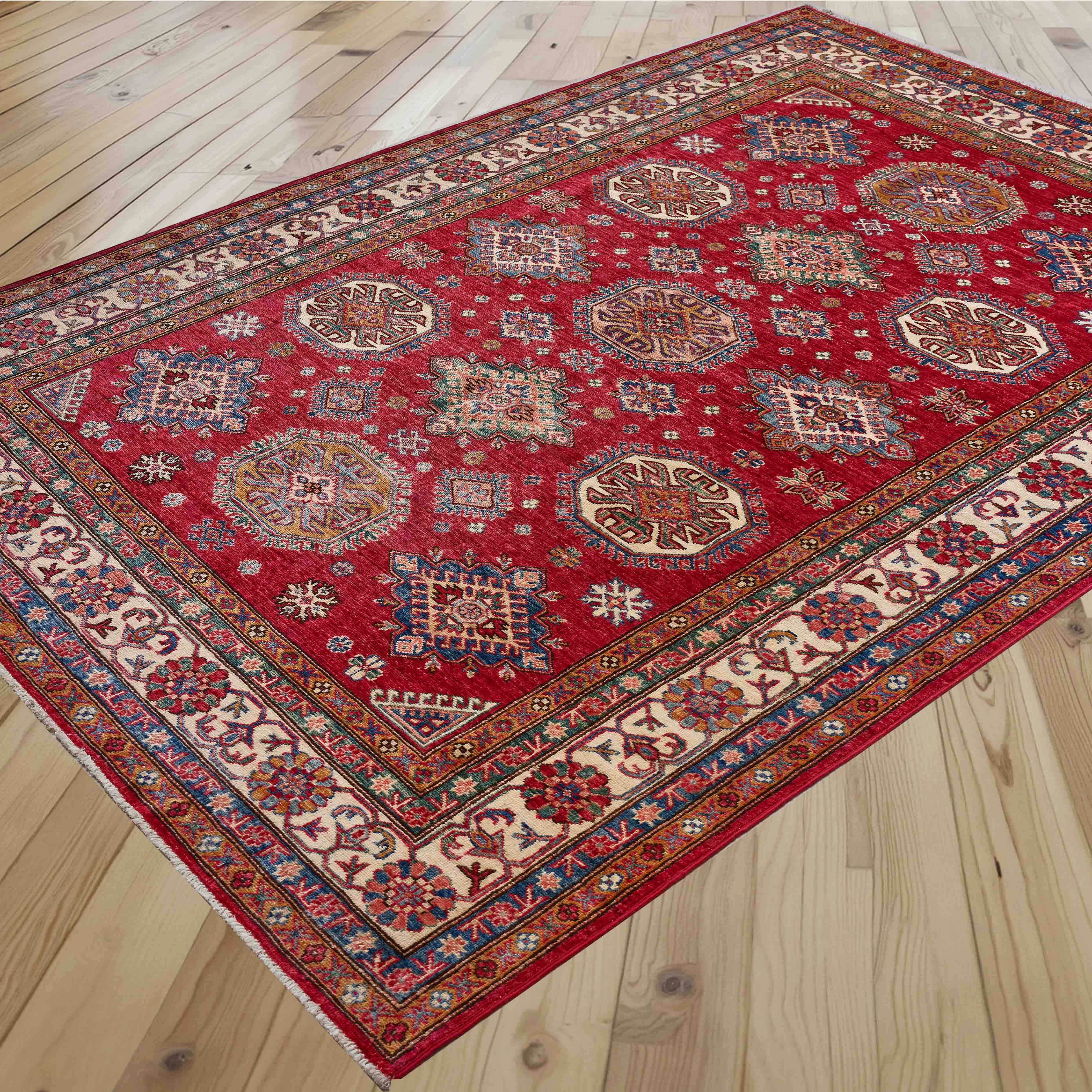A traditional Persian-style area rug with a vibrant red field and intricate geometric medallions, displayed on a light-colored wooden floor.