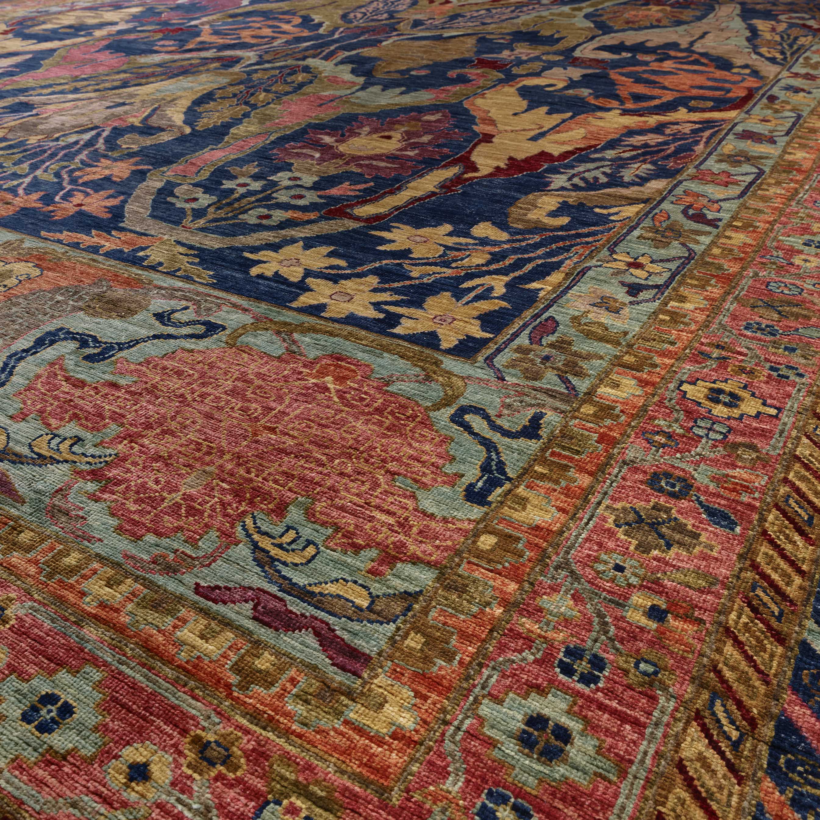 A close-up view of an Afghan carpet with a navy blue field, a large pinkish-red central medallion, and ornate borders in old gold, aqua and a soft pink red