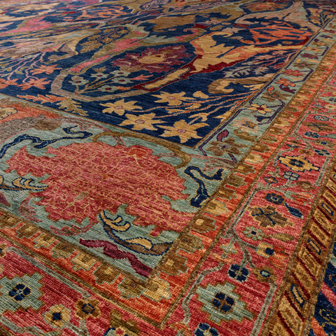 A close-up view of an Afghan carpet with a navy blue field, a large pinkish-red central medallion, and ornate borders in old gold, aqua and a soft pink red