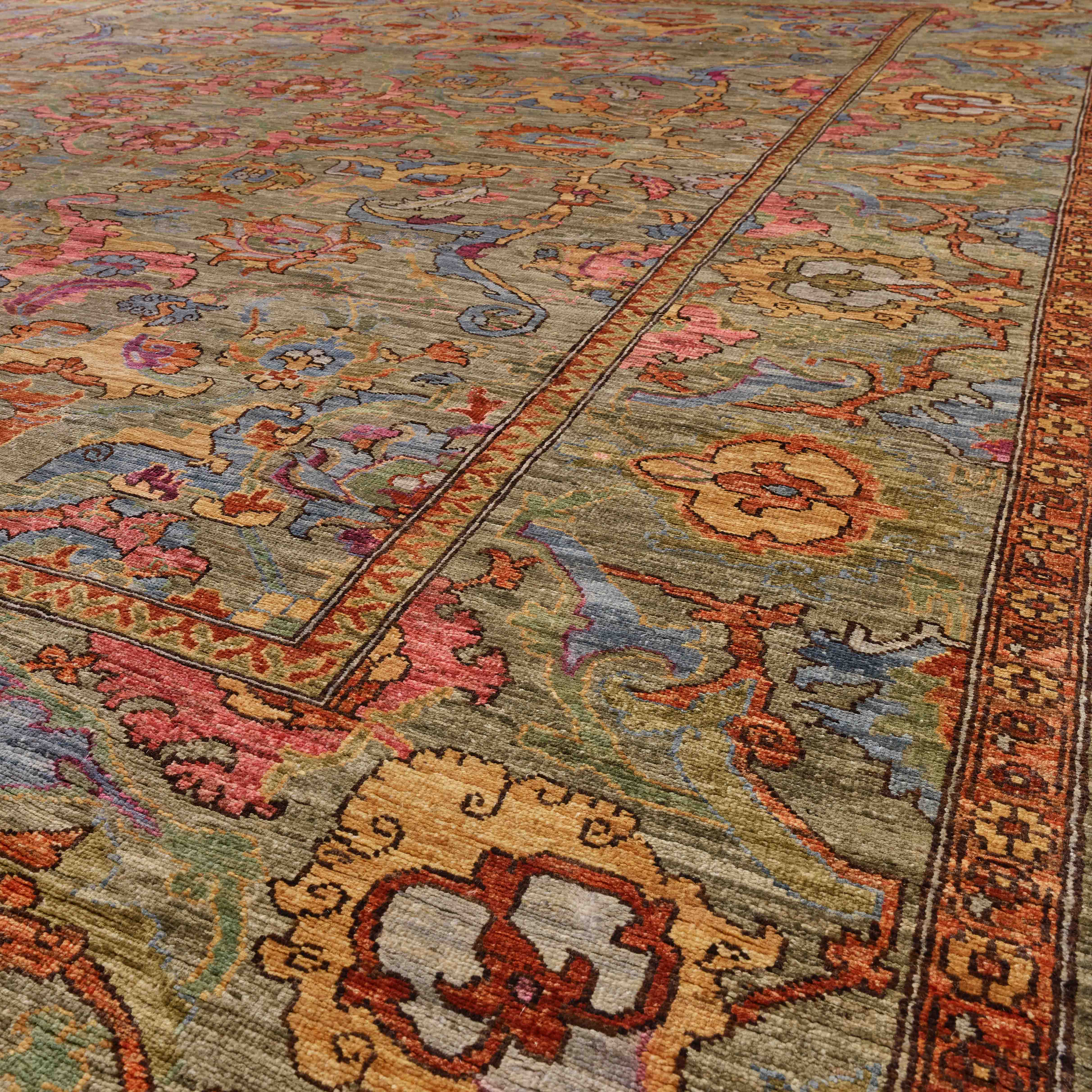 A close-up view of a traditional oriental-style area rug with an intricate floral pattern in muted tones of green, blush pink, golden wheat, peiwinkle blue and touches of burnt Sienna.