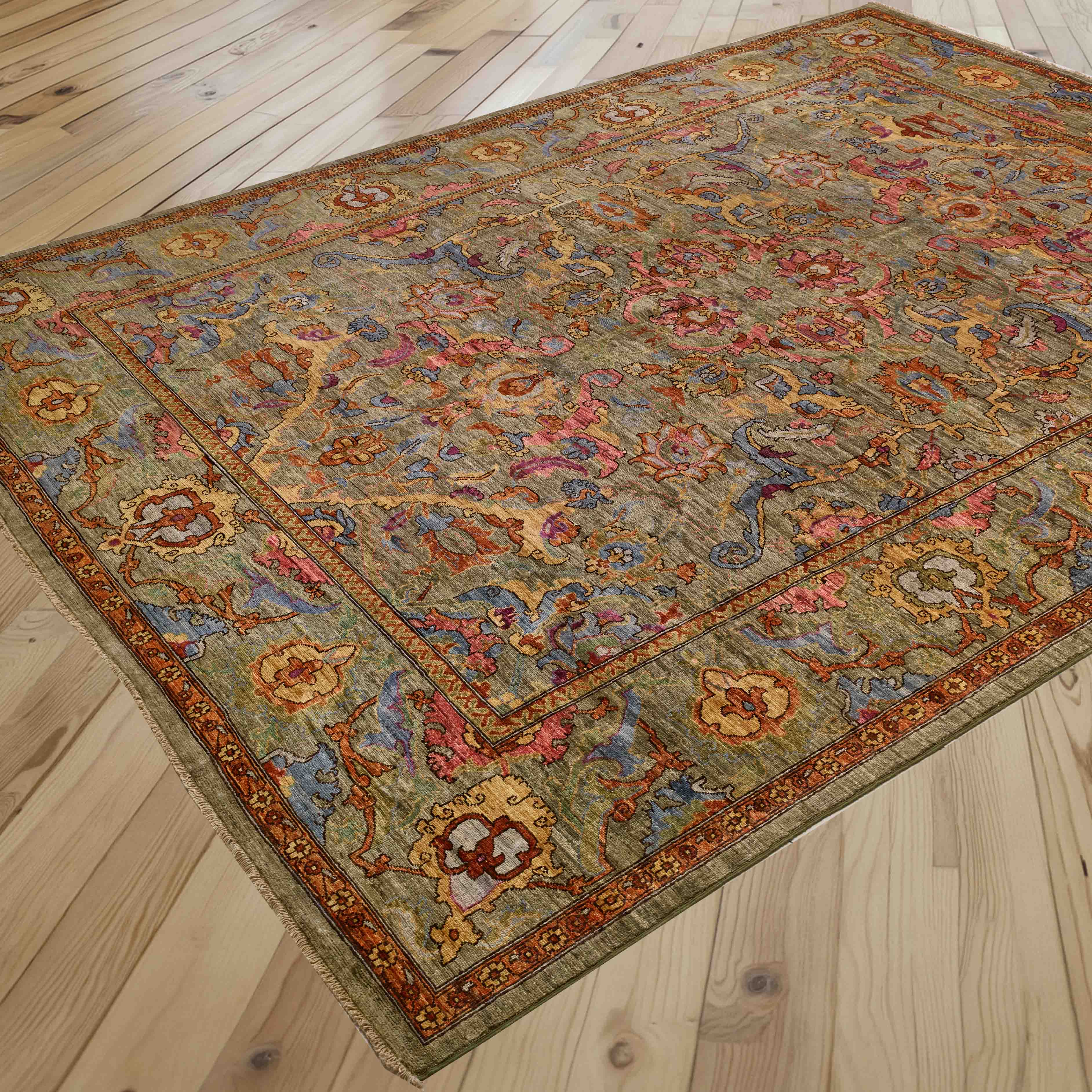 A traditional oriental area rug with an intricate floral pattern in muted tones of soft green, pale blue, honey, pink, and rust, shown laid out on a light wood plank floor.