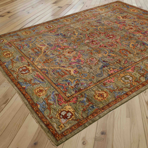 A traditional oriental area rug with an intricate floral pattern in muted tones of soft green, pale blue, honey, pink, and rust, shown laid out on a light wood plank floor.