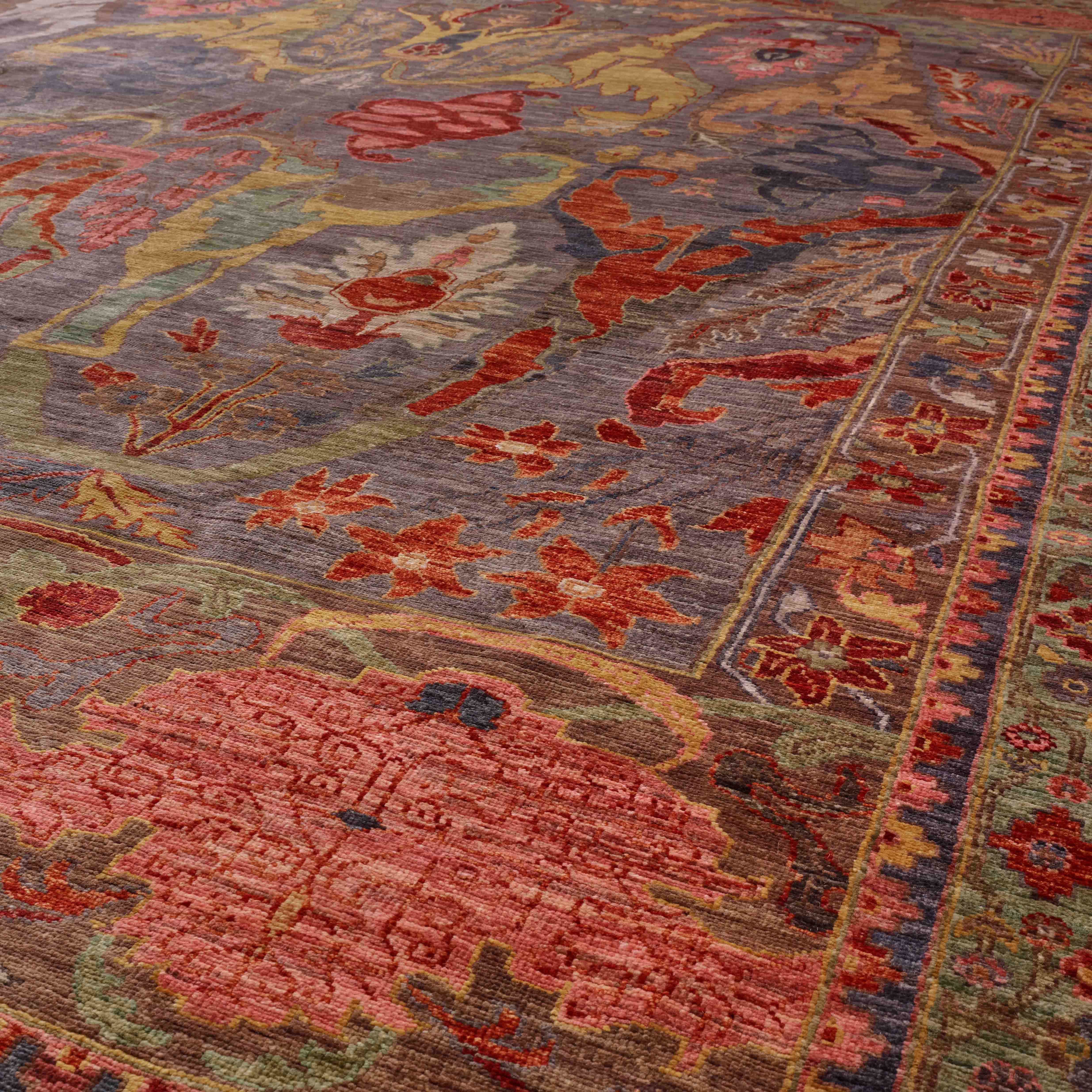 A close-up view of an ornate area rug with a distressed traditional pattern in grey tones, old rose pink, burnt orange, soft green, and pale gold.