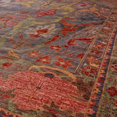 A close-up view of an ornate area rug with a distressed traditional pattern in grey tones, old rose pink, burnt orange, soft green, and pale gold.