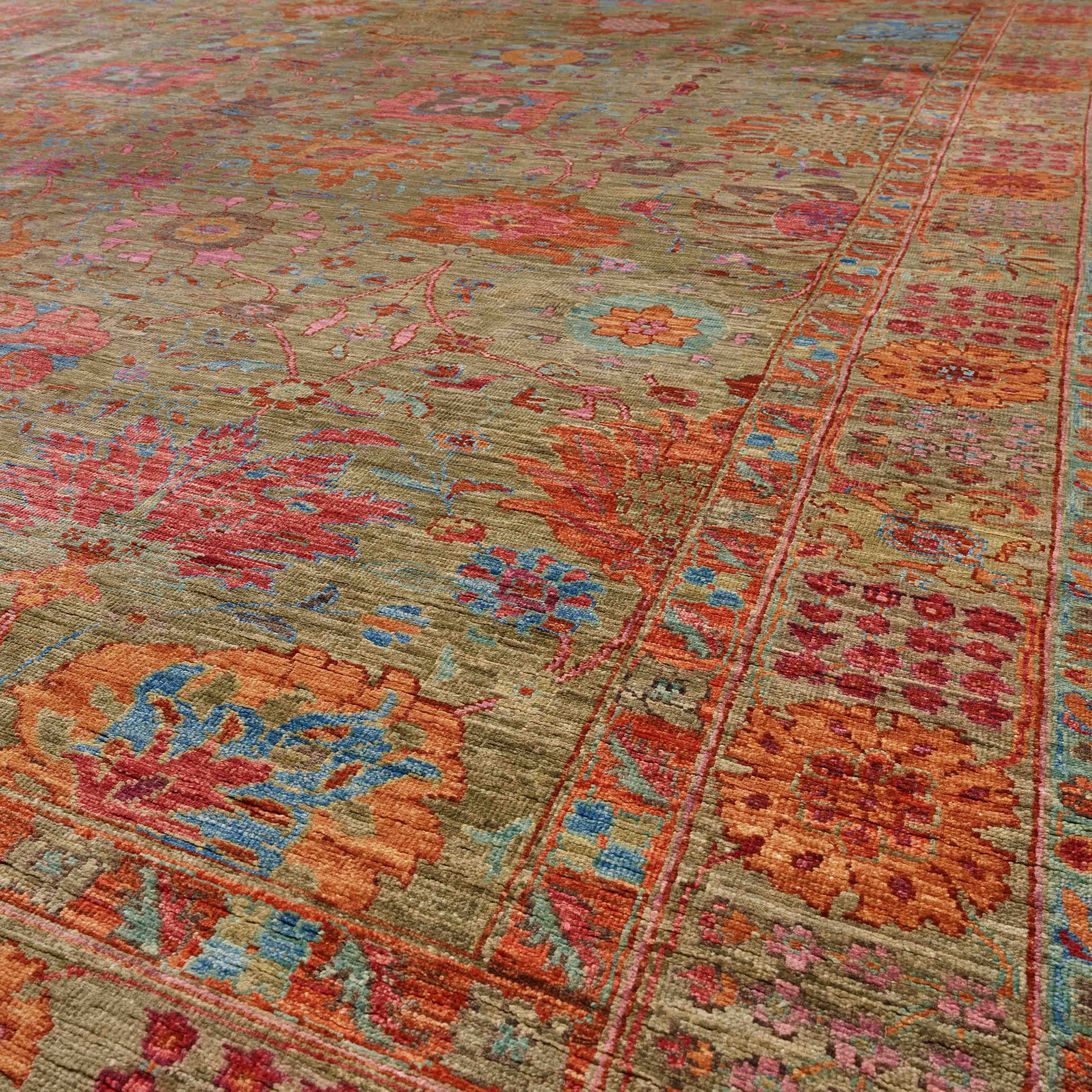 A close-up view of a traditional oriental-style area rug with an intricate floral pattern in muted tones of olive green, marmalade, crushed raspberry, terracotta, azure blue, and cranberry.