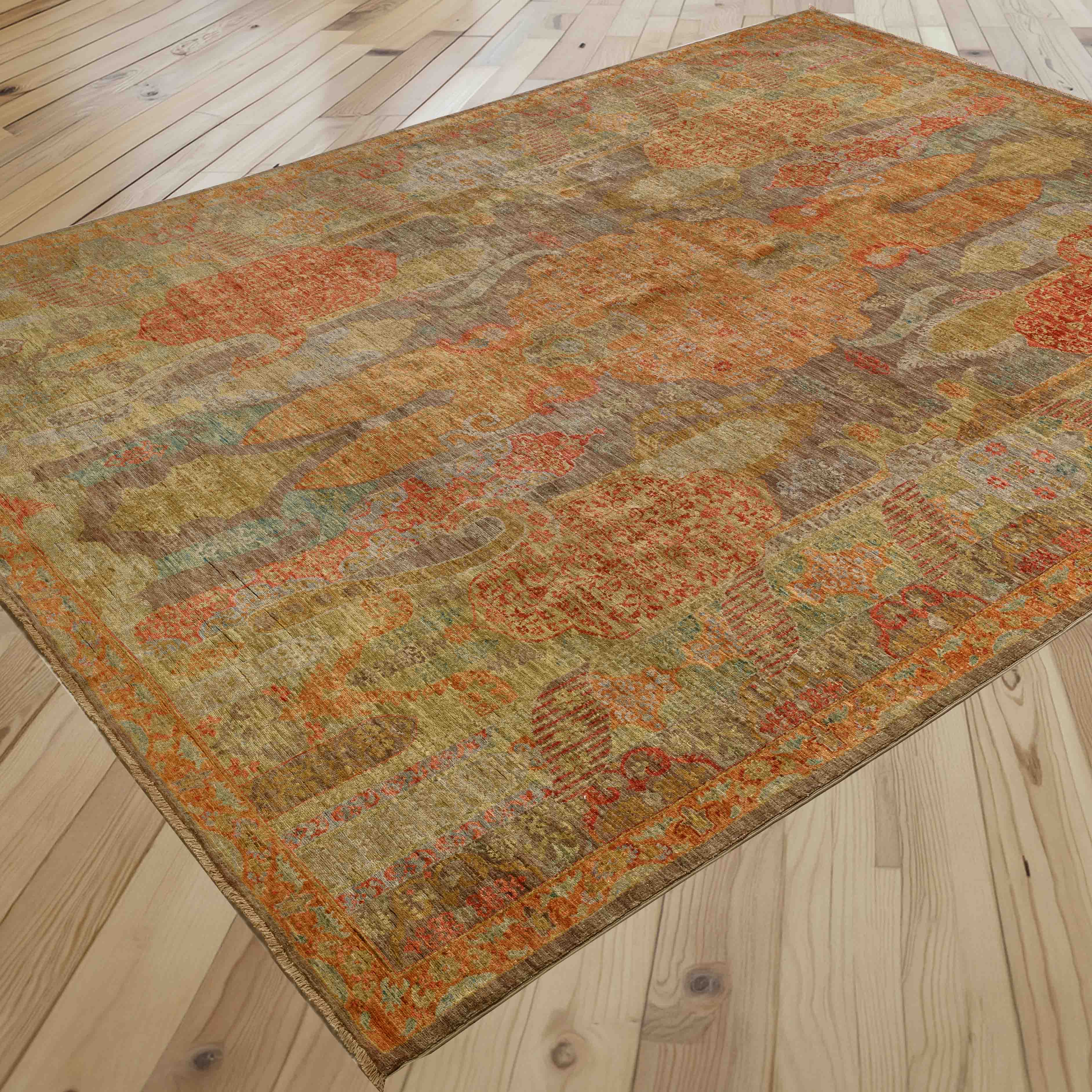 An area rug with an abstract, distressed pattern in warm earthy tones of orange, pale green, soft mocha, and brick red, shown laid out on a light wood plank floor.