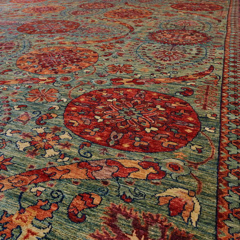 A close-up view of a patterned area rug with a blue/green base, featuring burnt Sienna and papaya floral motifs in a design that comes from Central Asia.