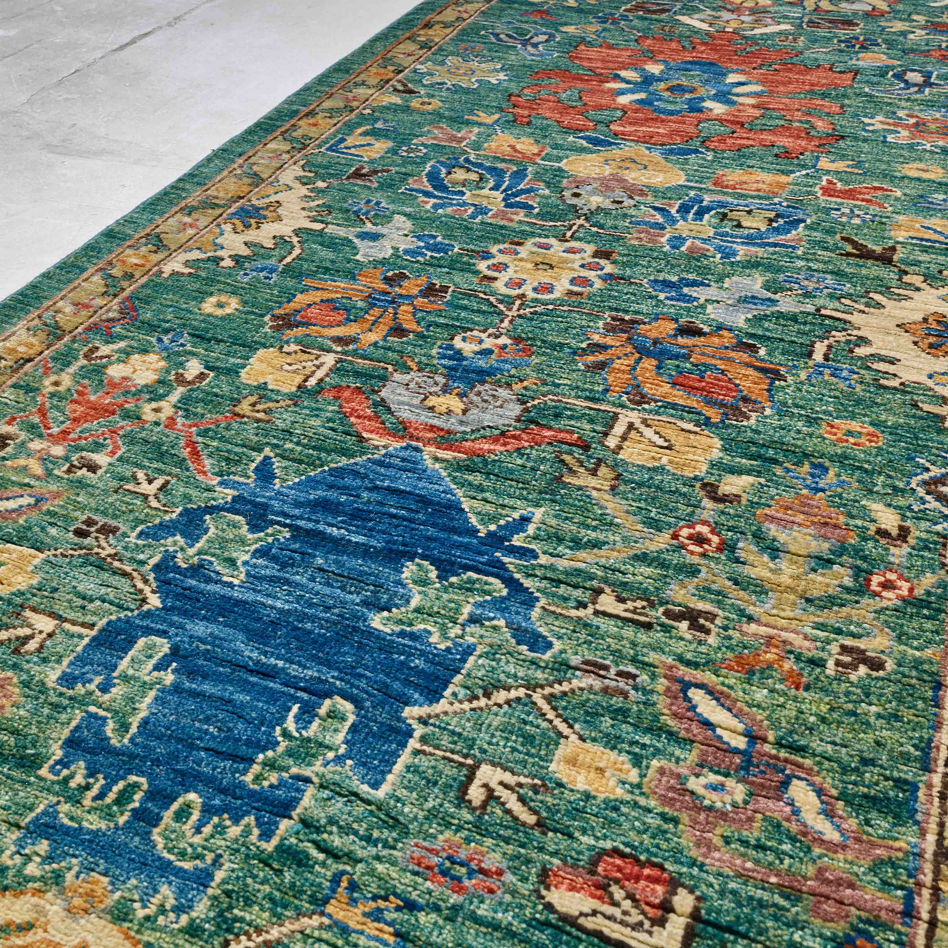A close-up of a traditional patterned runner with a teal-green field, featuring an azure-blue motif and floral motifs in papaya orange and honey.