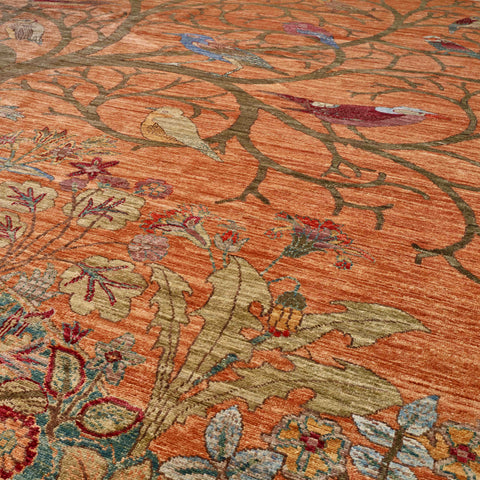 A close-up of an ornate area rug featuring a warm rust-orange background with intricate floral and branch patterns in muted green, beige, red, and blue.