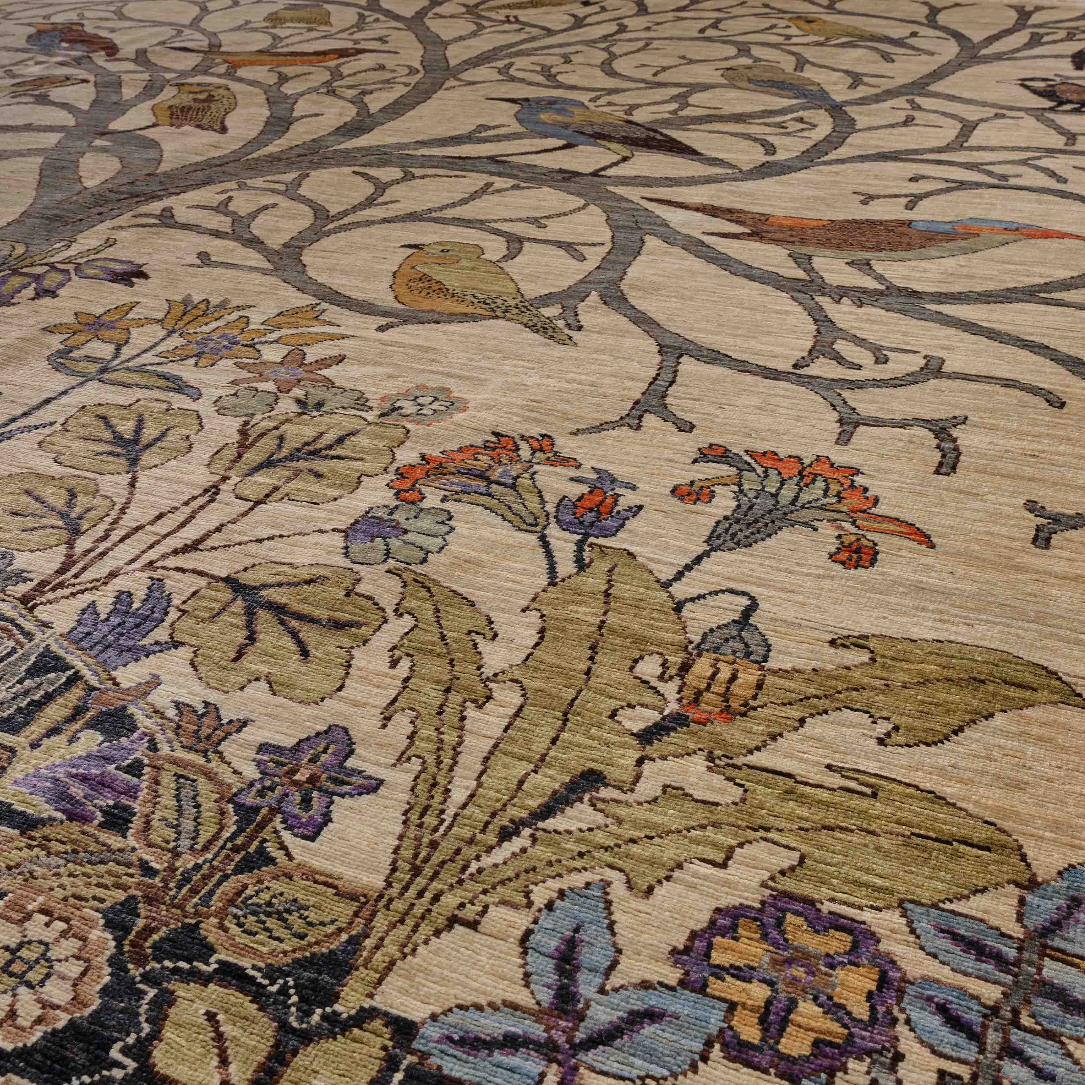 A close-up of a woven area rug featuring a detailed botanical and avian pattern with beige, olive green, blue, orange, and purple tones.