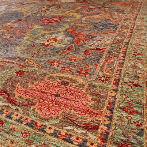A close-up view of an ornate traditional area rug with a distressed pattern in muted tones of burnt orange, soft grey, pale green, hibiscus, and gold.