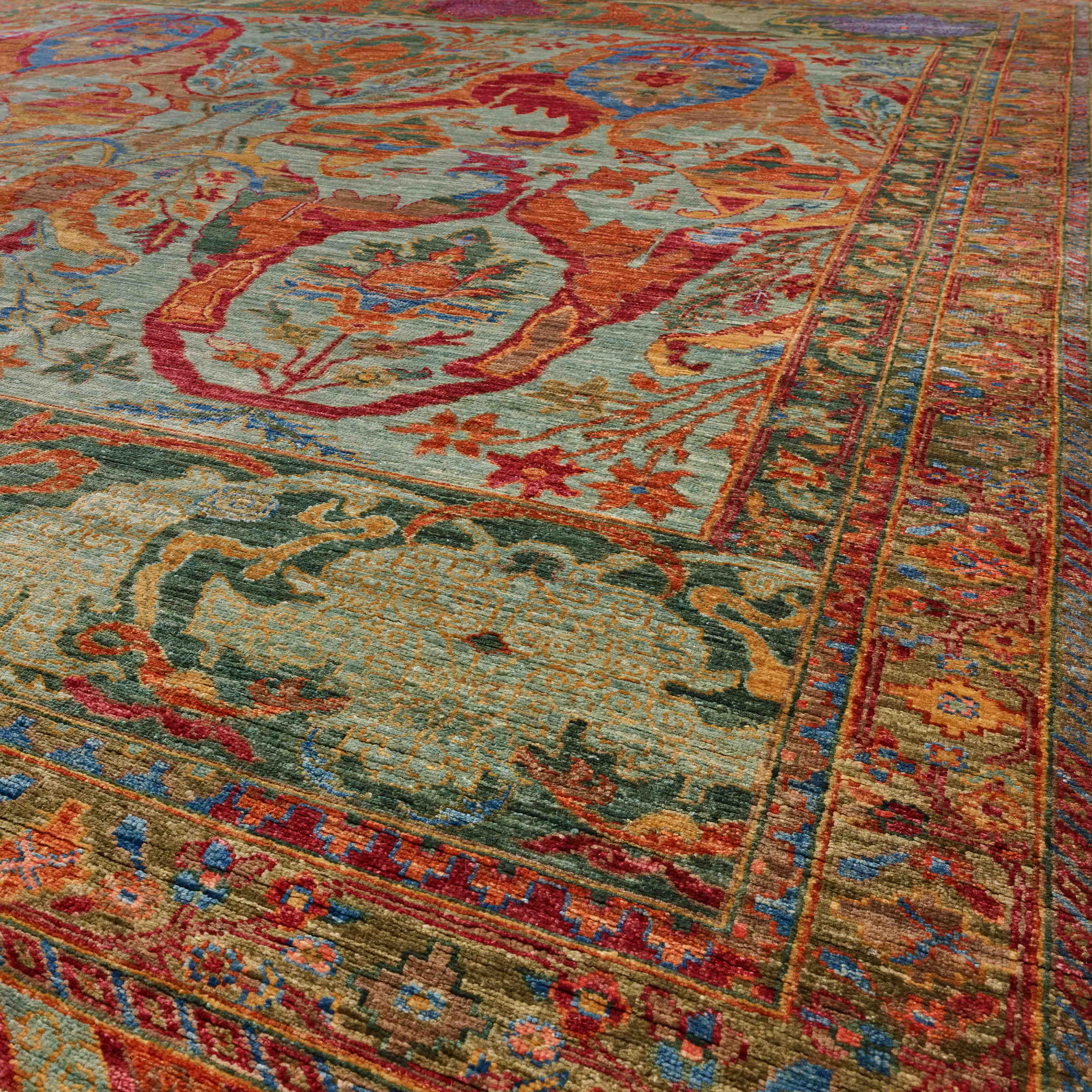 A close-up view of a traditional oriental-style area rug with a colour palette of greens, papaya, blue, crimson, gold and mocha.