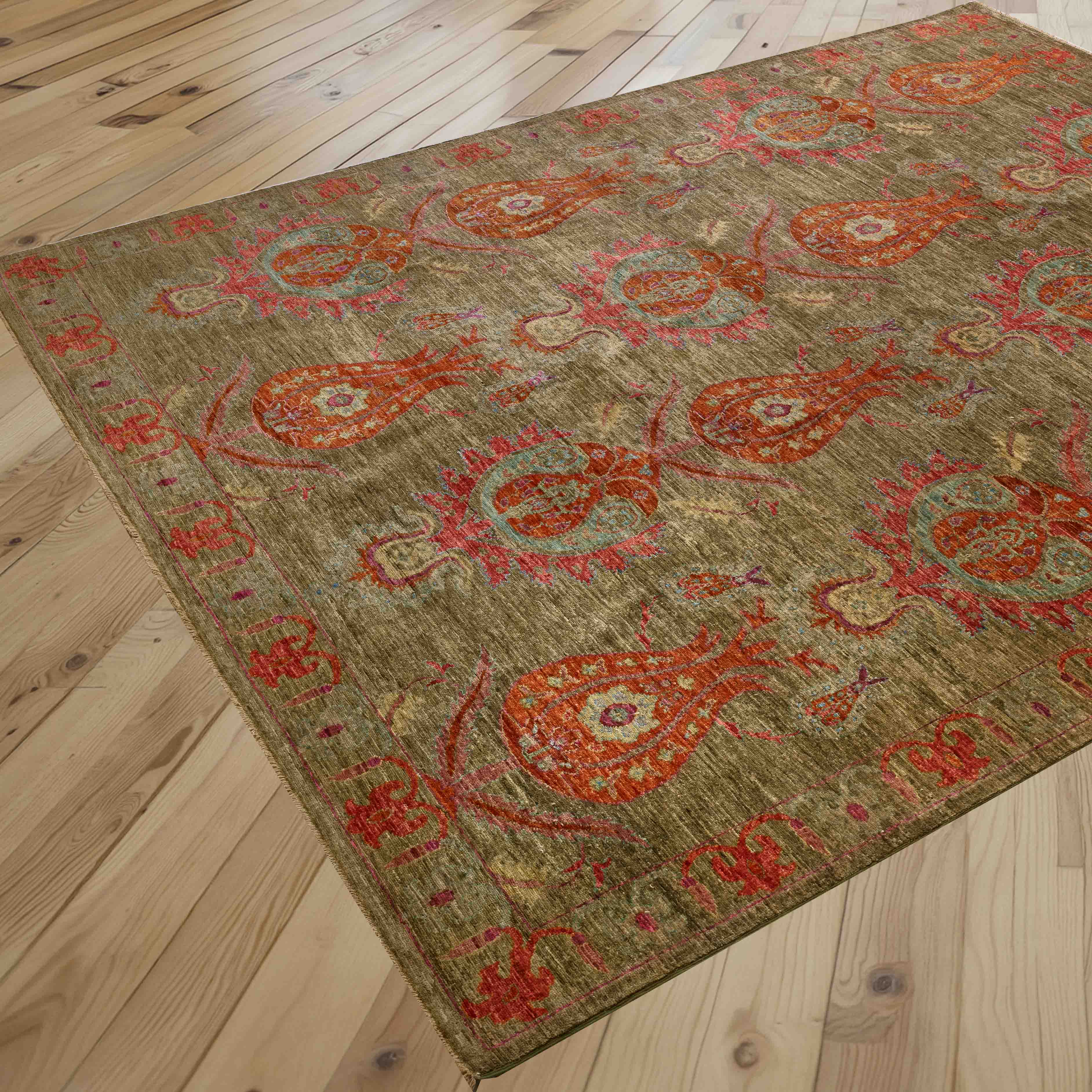 A rectangular area rug with an unusual pattern, shown laid out on a light-colored wooden plank floor. The rug features a muted olive-green base with prominent burnt orange and crushed raspberry tulips.