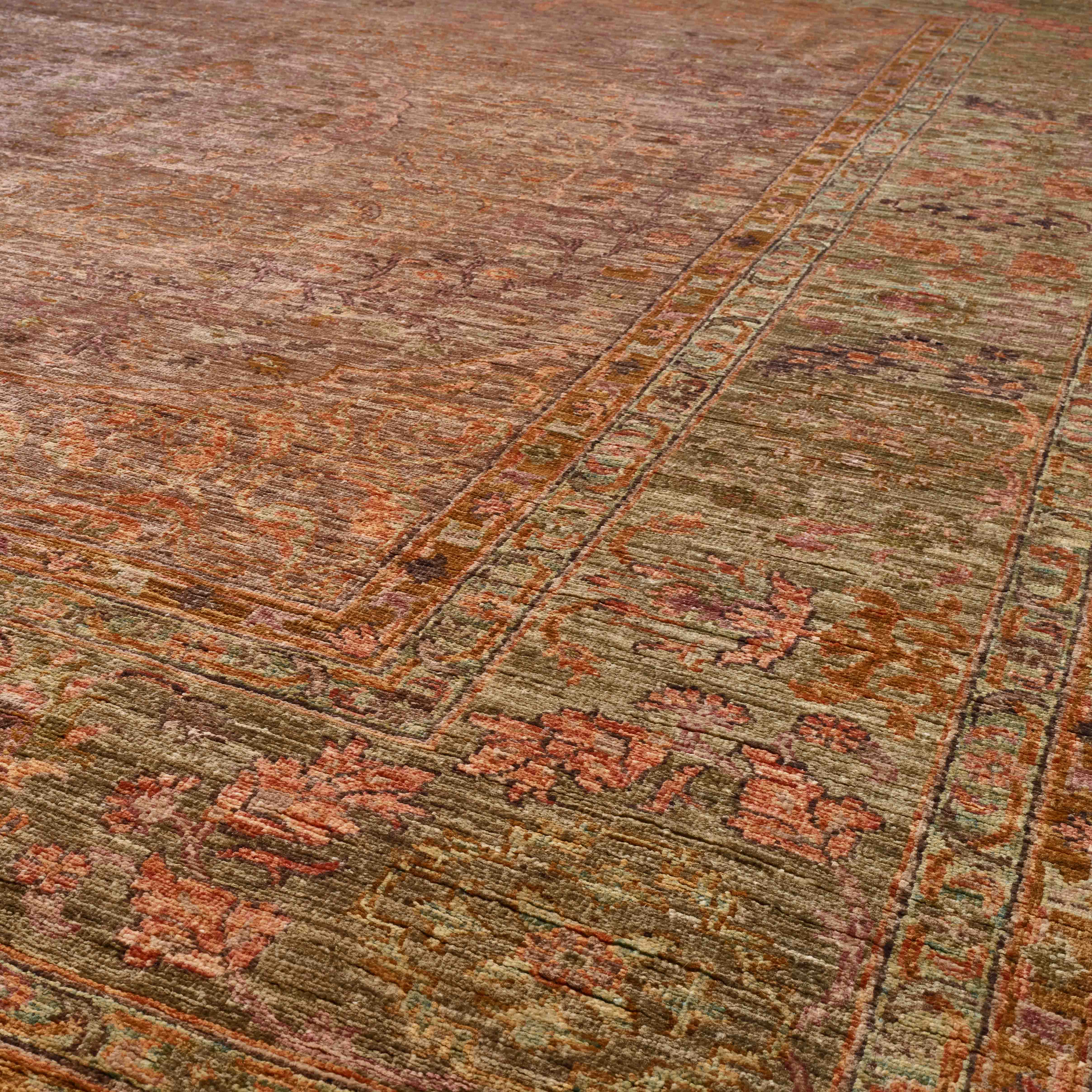 A close-up view of a distressed traditional area rug with an intricate pattern in muted tones of mink and soft olive green.
