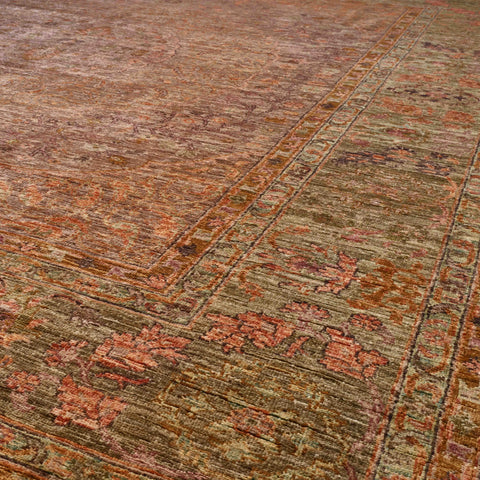 A close-up view of a distressed traditional area rug with an intricate pattern in muted tones of mink and soft olive green.