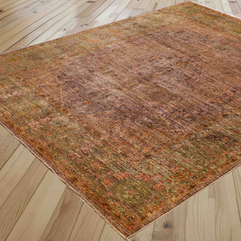 An antique-style distressed area rug with a complex multicolor pattern in shades of mink and soft olive green, shown laid out on a light-colored wooden plank floor.