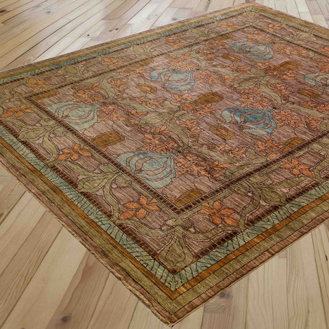 A rectangular area rug with an ornate floral and vine pattern, shown laid out on a light-colored wooden plank floor. The rug features a warm brown base with prominent orange, sage green, and light blue accents.