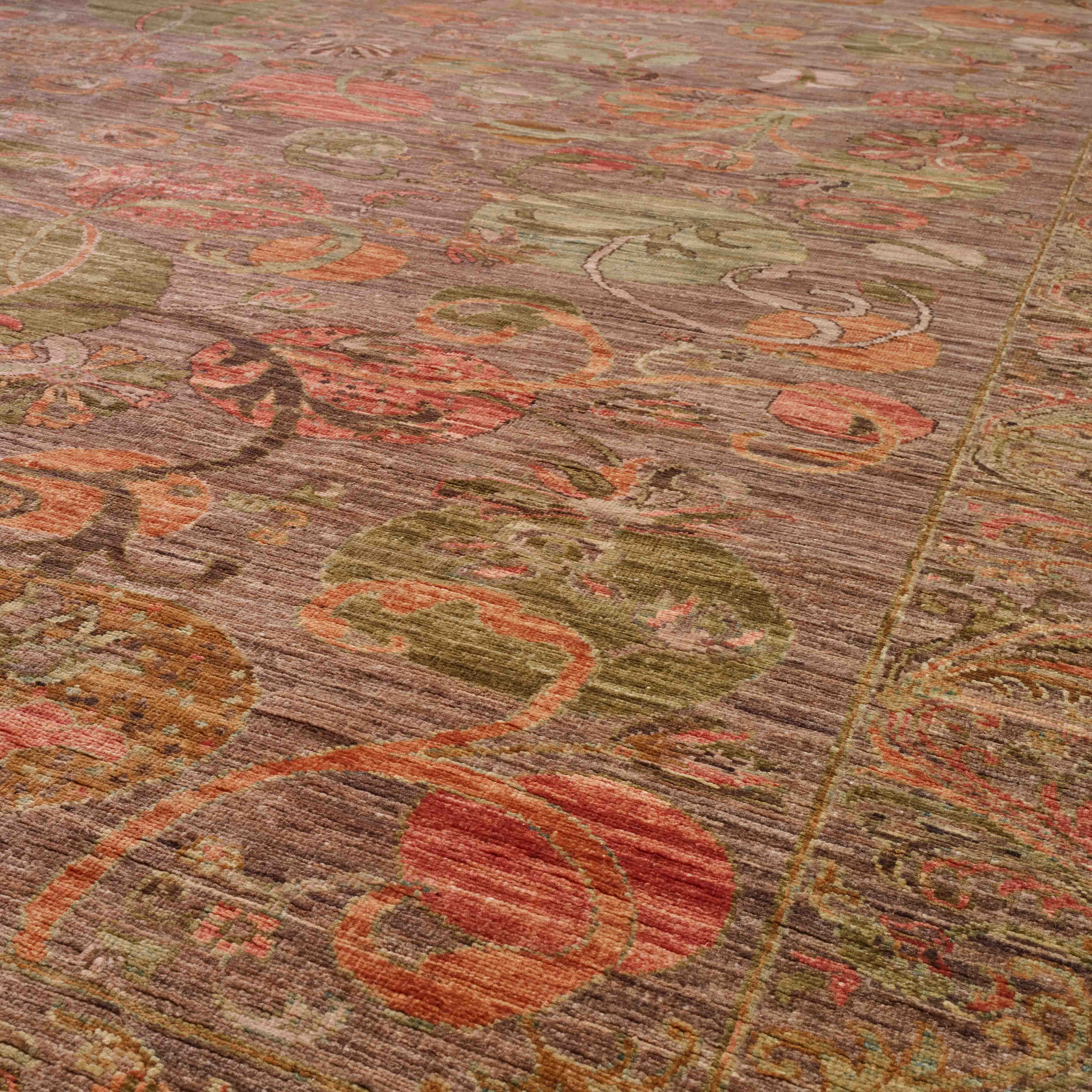 A close-up view of an ornate area rug with a distressed traditional pattern in muted tones of brown, rust red, sage green, and beige.