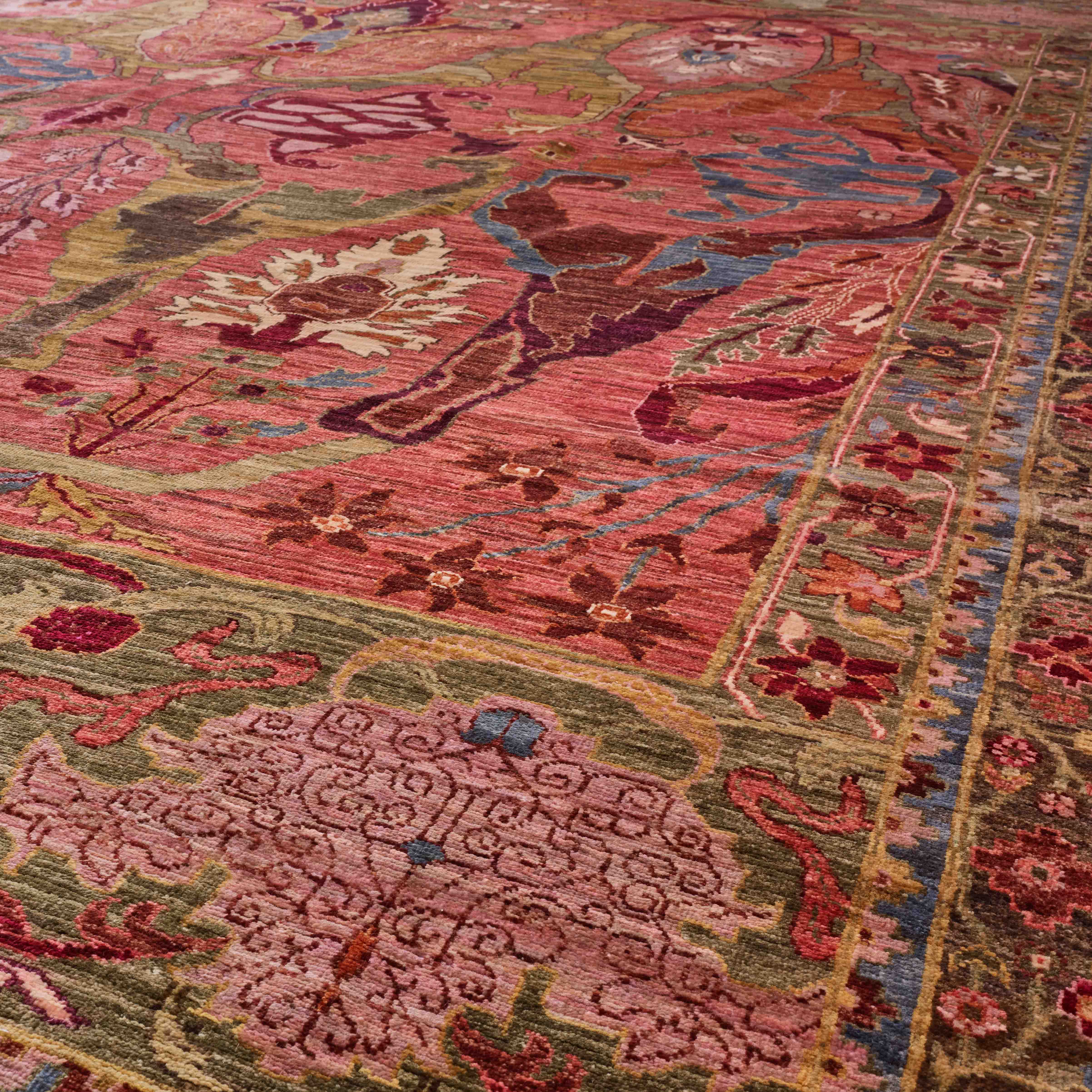 A close-up view of a traditional oriental-style area rug with an intricate floral and geometric pattern in dusty pink, red, olive green, blue, and sand tones.