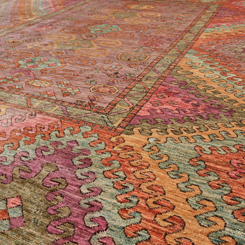 A close-up of a multicoloured patterned area rug with intricate geometric and tribal-inspired motifs in dusty pink, terracotta orange, sage green, and muted purple.