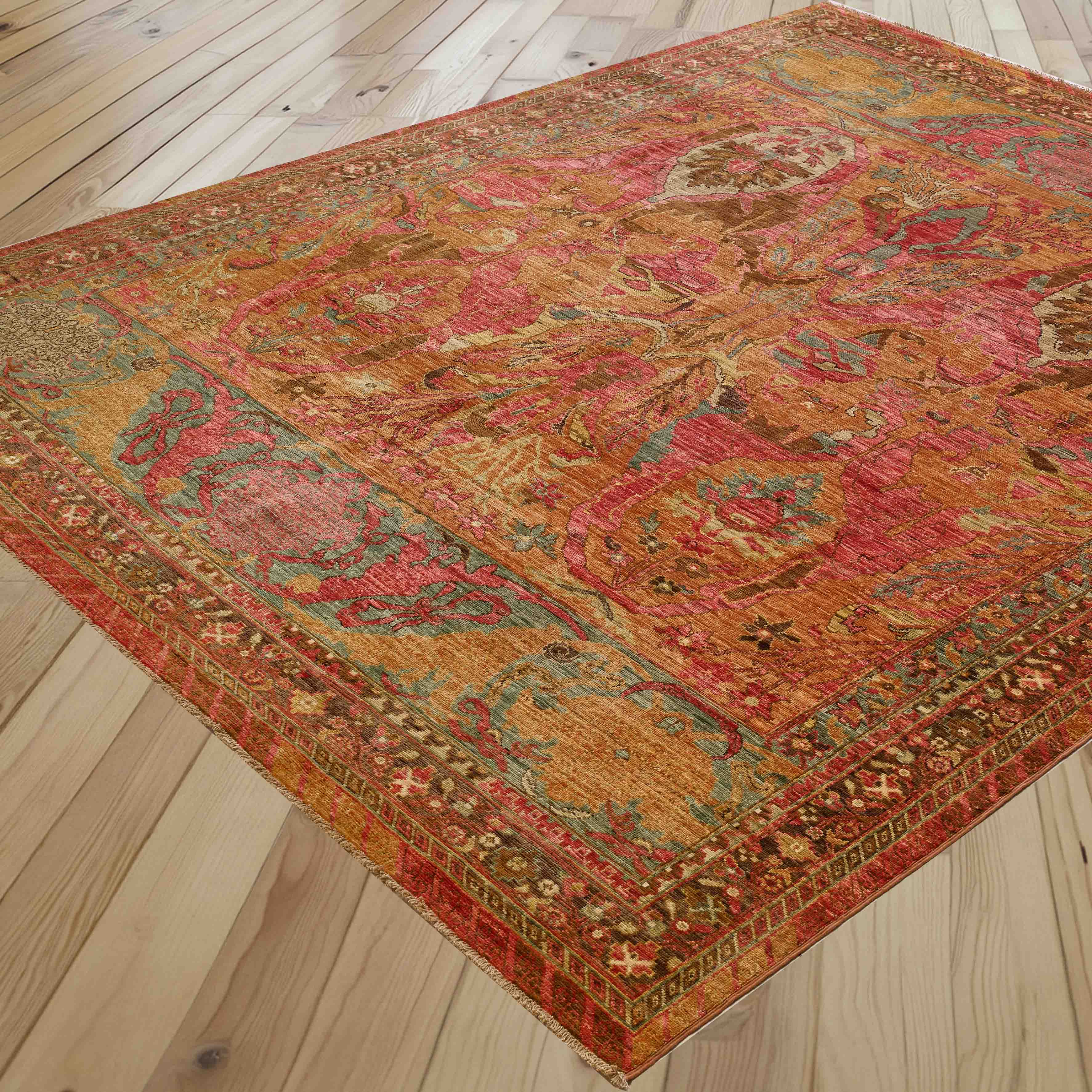 A rectangular vintage-style area rug with an intricate medallion pattern in red, gold, teal, and brown, shown laid out on a light-colored wooden plank floor.