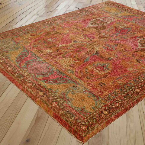 A rectangular vintage-style area rug with an intricate medallion pattern in red, gold, teal, and brown, shown laid out on a light-colored wooden plank floor.