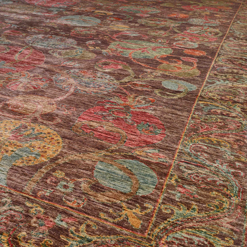 A close-up view of an ornate area rug with a distressed traditional pattern in brown, red, teal, and gold tones.