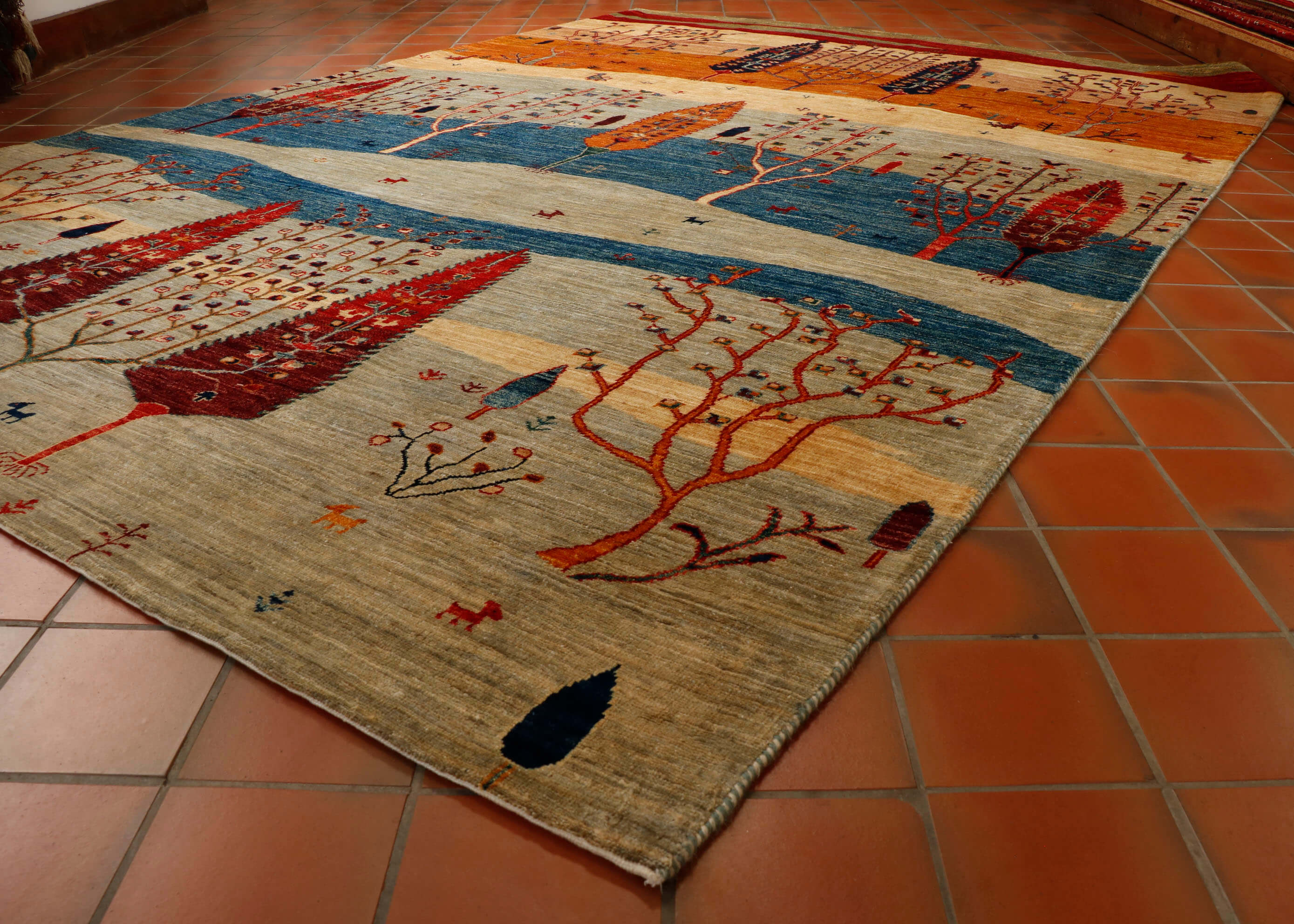 Stylised tree design Afghan rug in colourings of pale grey, mid blue, old gold, cream and brick red.