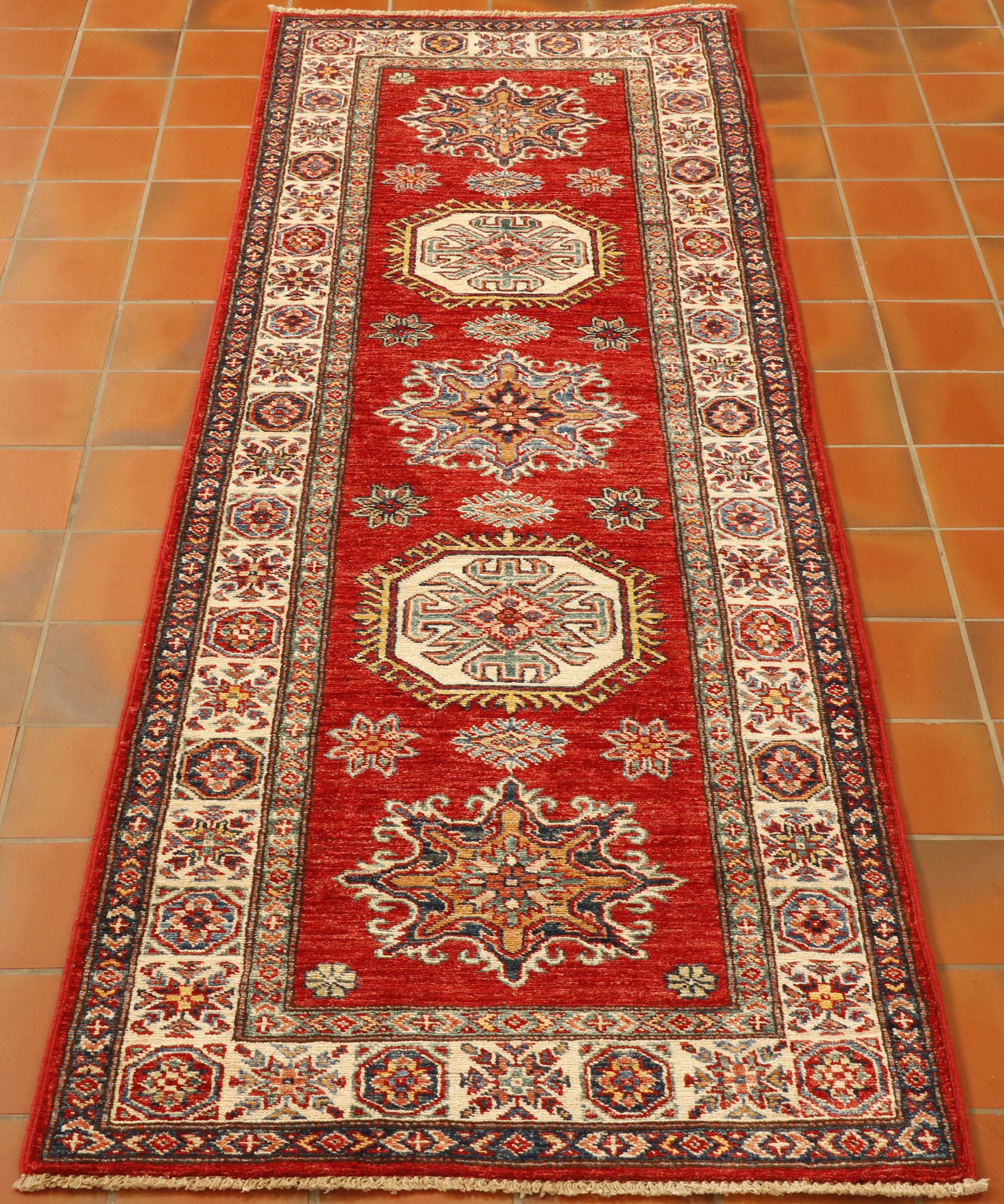 A rich tomato background with an ivory border and gold, light blue and dark blue have been used in this fine Afghan Kazak runner.